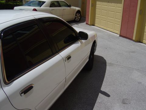 2000 Ford Crown Victoria - A white sedan is parked in front of a garage, with another white sedan visible in the background.