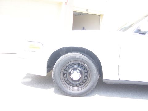 2000 Ford Crown Victoria - A close-up view of the front passenger side of a white sedan, showing the wheel and part of the fender.