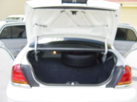 2000 Ford Crown Victoria - Open trunk of a 2000 Ford Crown Victoria, revealing the spare tire and interior space. Another vehicle is partially visible.