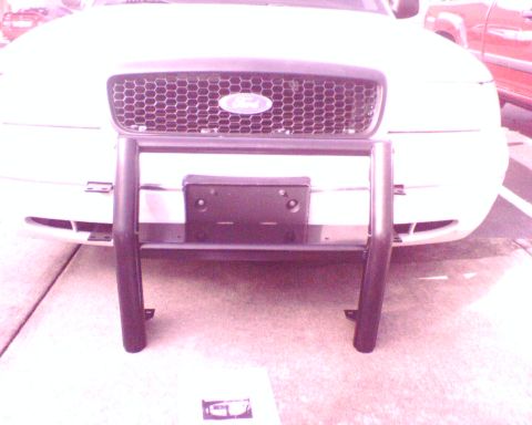 2000 Ford Crown Victoria - A black tubular push bar with a bolt-on license plate bracket stood upright on the driveway against the front of a white Ford sedan for a t…