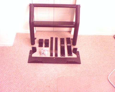 2000 Ford Crown Victoria - A black Setina push bumper and its associated mounting hardware are displayed on a carpeted floor, likely for installation.