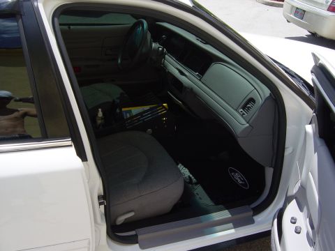 2000 Ford Crown Victoria - The interior of a white Ford Crown Victoria is shown, gray seats and a black dashboard with a Ford logo on the floor mat.