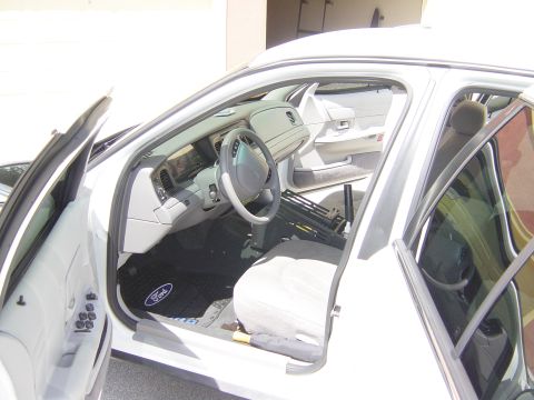2000 Ford Crown Victoria - The interior of a white sedan is shown with the driver's side door open. A Ford logo is visible on the floor mat.
