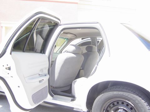 2000 Ford Crown Victoria - The interior of a white sedan is visible with the front and rear doors open, revealing grey cloth seats.