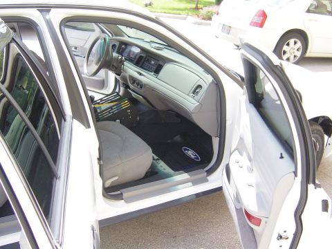 2000 Ford Crown Victoria - The interior of a white 2000 Ford Crown Victoria is shown with the front passenger door open, revealing the dashboard and seats.
