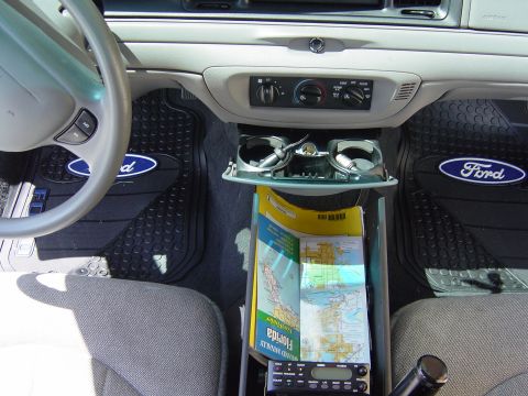 2000 Ford Crown Victoria - Looking down at the footwell and center stack of a light-grey Ford sedan interior, showing the rotary HVAC controls, a fold-down cup holder…