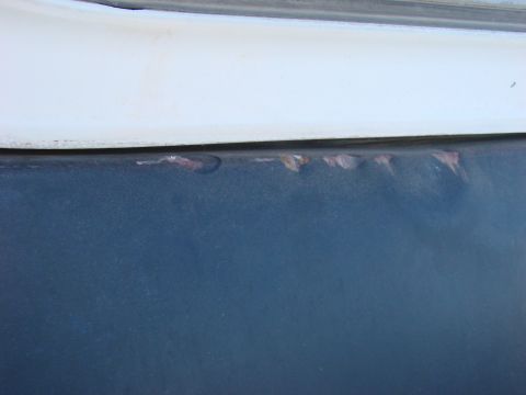 1979 Ford Bronco - Rust spots are visible on the lower panel of a vehicle, beneath a white trim piece.