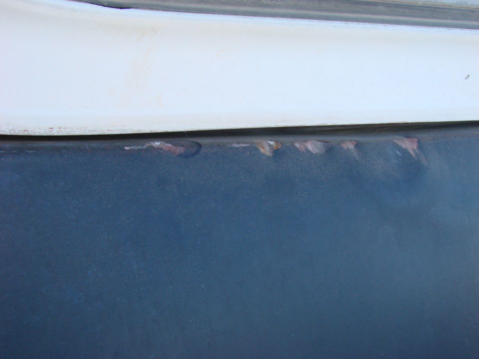 Rust spots on dark blue vehicle panel below white trim