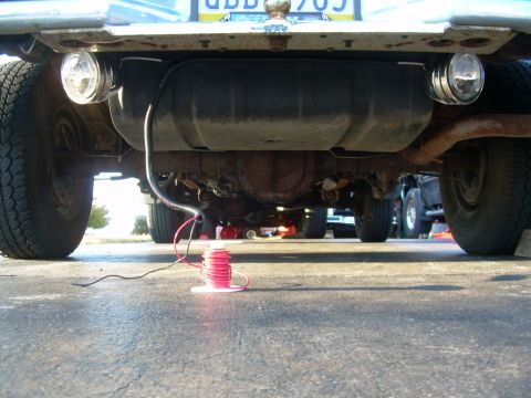 1988 Ford Bronco - Wiring is being installed on the underside of a vehicle, with a fuel tank and exhaust system visible.