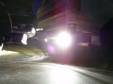 1988 Ford Bronco - Bright reverse lights shine down on a wet asphalt surface, illuminating the vehicle's exhaust system.