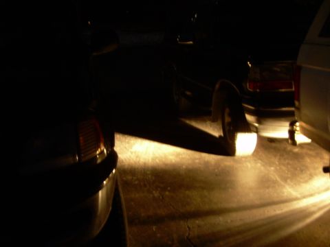 1988 Ford Bronco - Two SUVs are parked at night, with the reverse lights of the dark SUV illuminated.