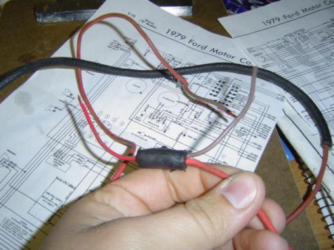 1979 Ford Bronco - A hand holds a wiring harness over electrical schematics for a 1979 Ford vehicle.