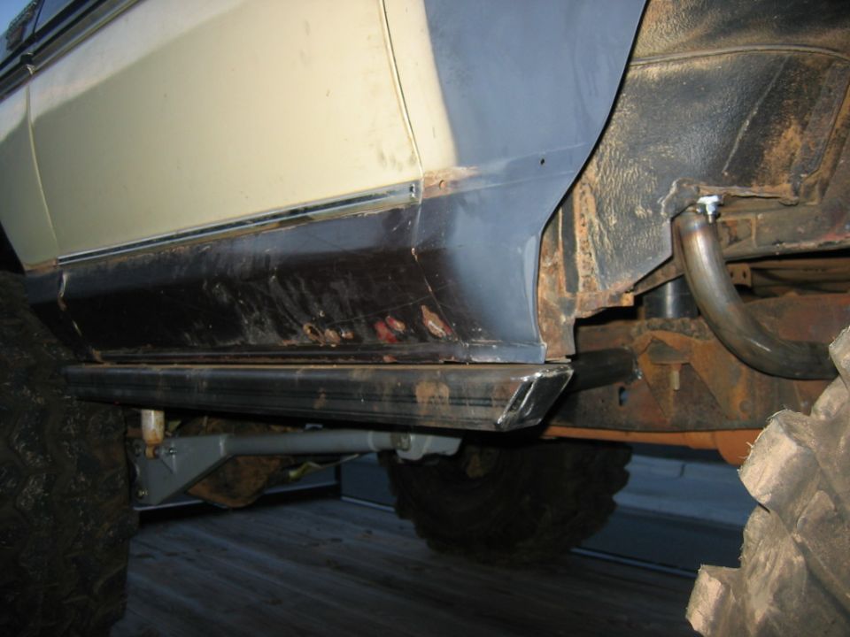 Off-road vehicle side showing rust and custom metal rock sliders installed below the rocker panel