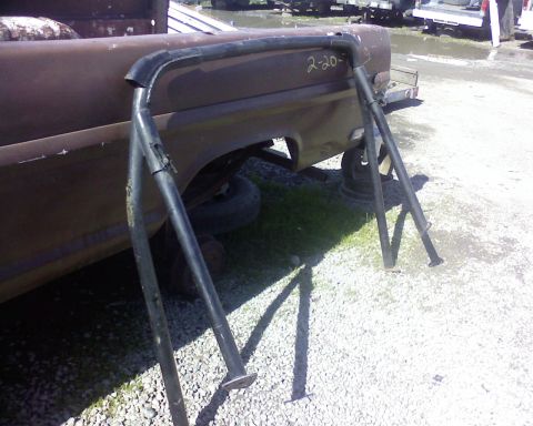 1995 Ford Bronco - A roll bar is shown next to the bed of a rusty truck, with '2-20-' written on the truck's side.