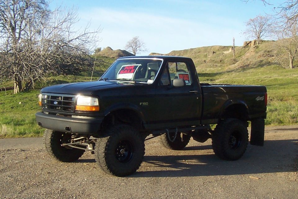 Black 1994 Ford F-150 pickup truck with lifted suspension and off-road tires. 'For Sale' sign in windshield