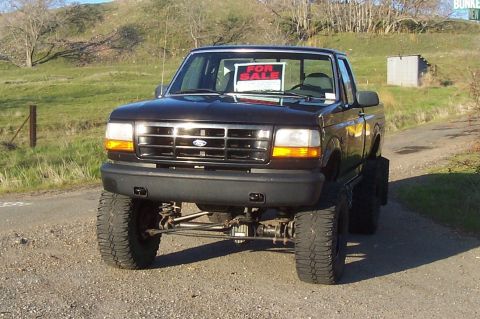 1994 Ford F-150 - This black 1994 Ford F-150 pickup truck is shown from the front, a lifted suspension and large off-road tires.