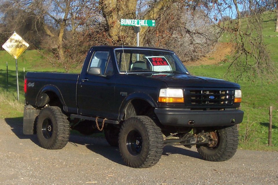 Black 1994 Ford F-150 pickup truck with lifted suspension and large tires, parked on a dirt road
