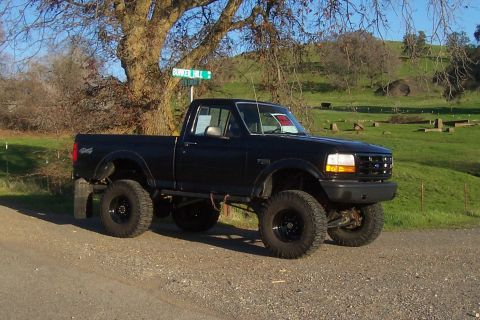 1994 Ford F-150 - This lifted pickup truck is parked on a dirt road with a rural landscape in the background.