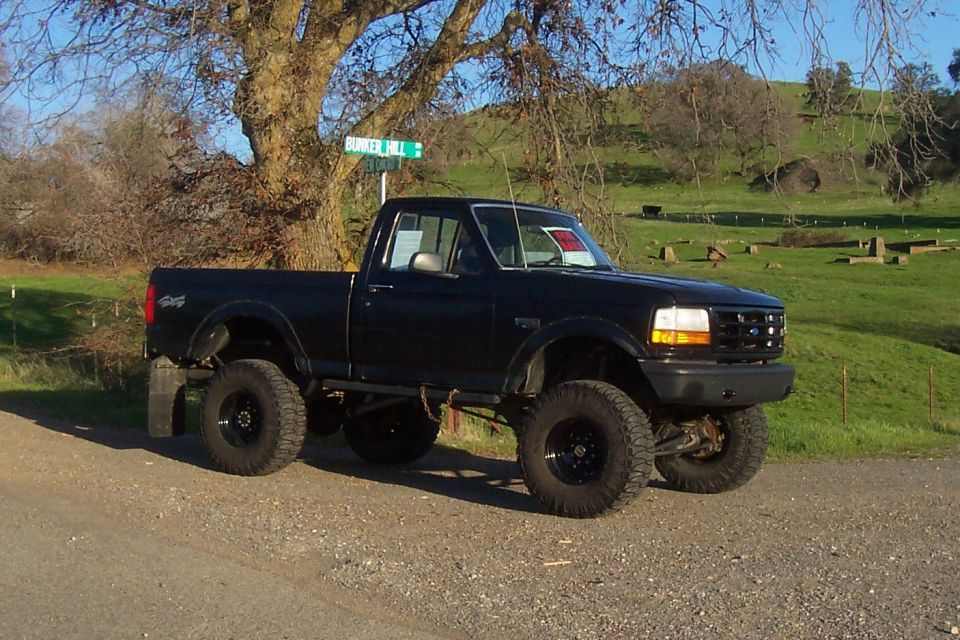 Black lifted pickup truck parked on a dirt road with a tree and a street sign
