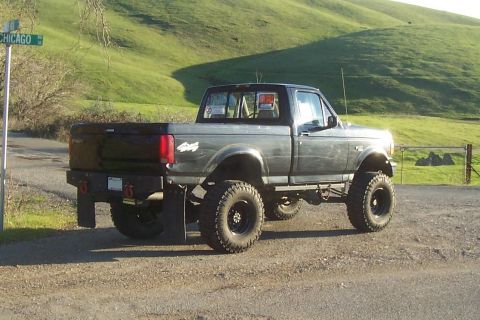 1994 Ford F-150 - This lifted 1994 Ford F-150 pickup truck is parked on a dirt road with grassy hills in the background.