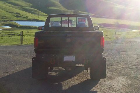 1994 Ford F-150 - Rear view of a dark pickup truck with a 'For Sale' sign visible in the back window, parked outdoors.