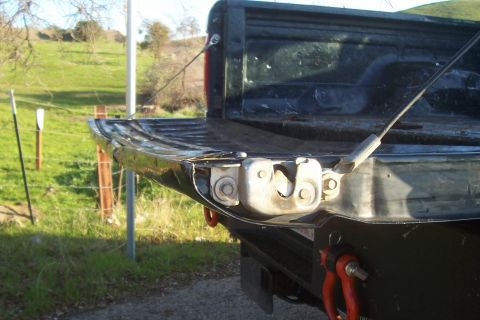 1994 Ford F-150 - The tailgate latch mechanism of a black Ford F-150 is visible from the rear, with a rural landscape in the background.