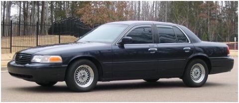 1999 Ford Crown Victoria - Dark blue 1999 Ford Crown Victoria sedan with aftermarket wheels parked outdoors.