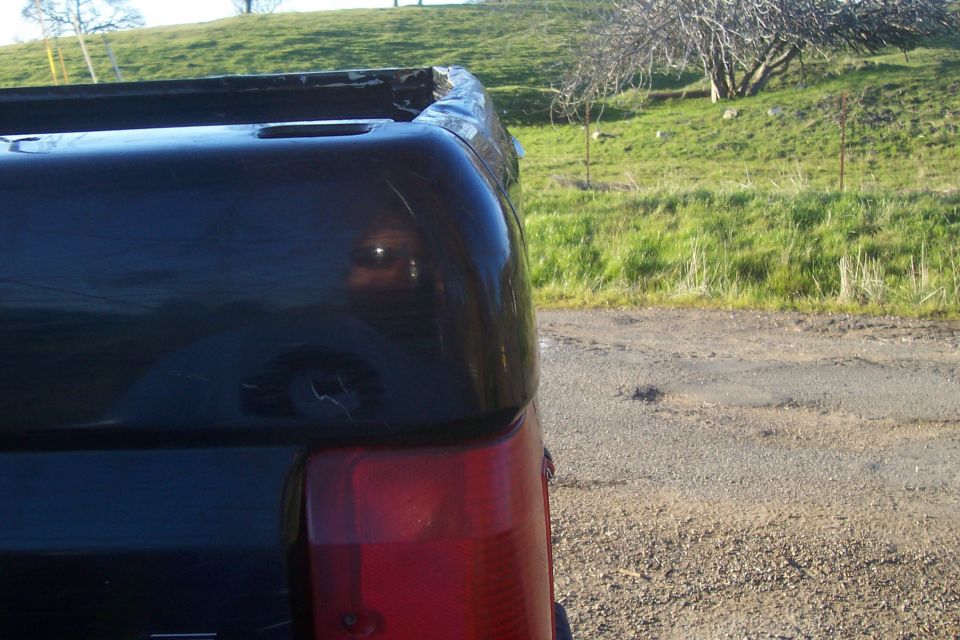 Black pickup truck rear corner, showing taillight and bed rail. The truck appears to be from the early to mid-1990s