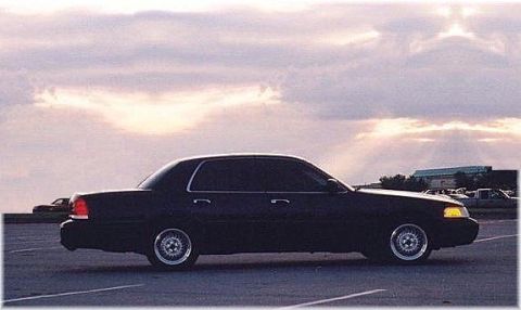 1999 Ford Crown Victoria - Side view of a black sedan with aftermarket wheels parked outdoors.