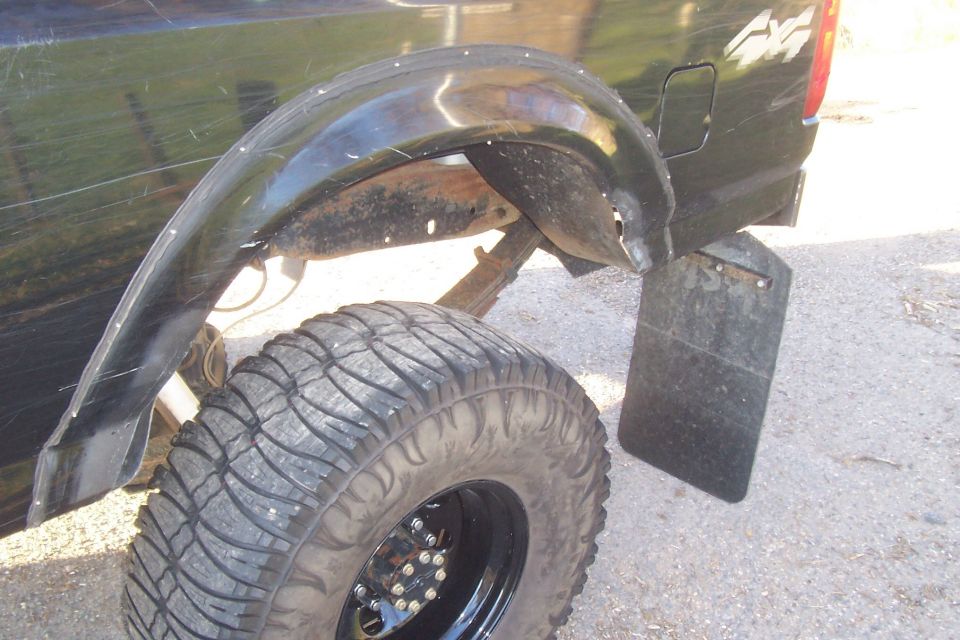 Rear fender and large off-road tire on a black truck. Mud flap visible