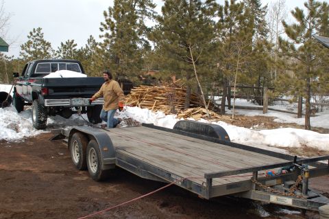 1985 Chevrolet C/K Pickup - A man attaches a trailer to a black pickup truck in a snowy, wooded environment.