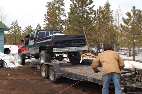 1985 Chevrolet C/K Pickup - A lifted 1985 Chevrolet C/K Pickup is winched onto a trailer in a snowy, rural setting.