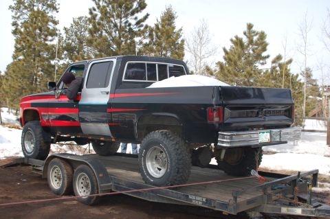 1985 Chevrolet C/K Pickup - This lifted Chevrolet C/K Pickup truck is loaded onto a trailer, showing its custom paint job and off-road tires.