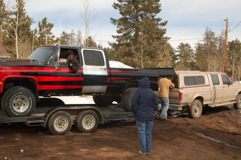 1985 Chevrolet C/K Pickup - A black and red pickup truck is being loaded onto a tan pickup truck via a trailer.