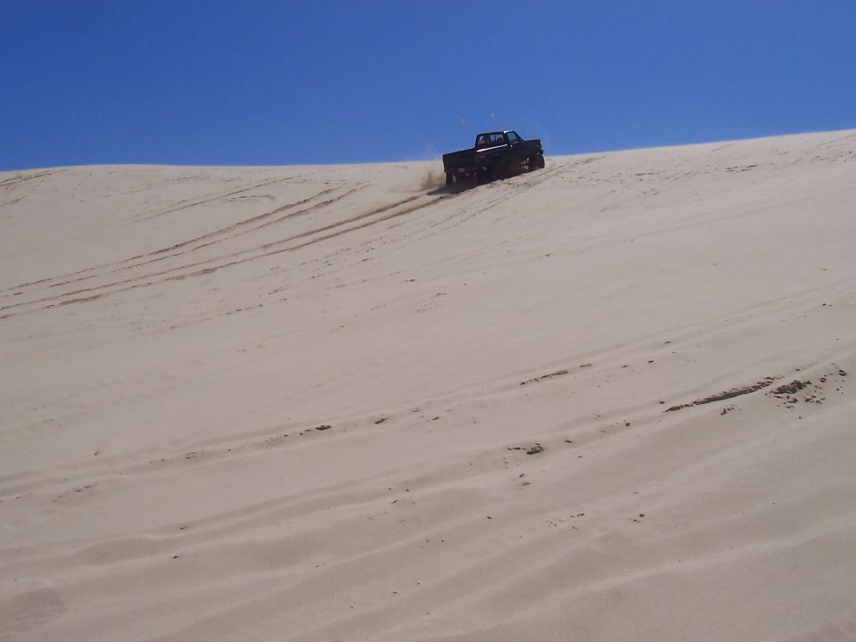 Black pickup truck driving up a sand dune
