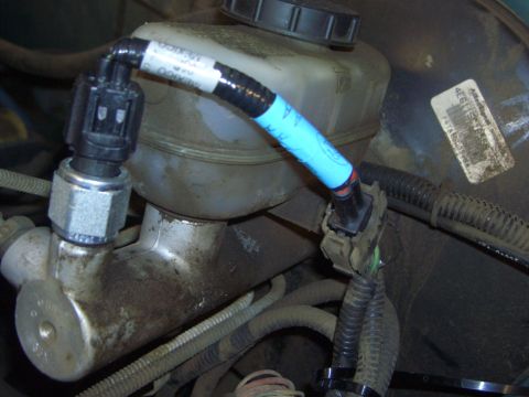1996 Ford Bronco - Close-up of a vehicle's brake fluid reservoir and associated sensor with wiring.