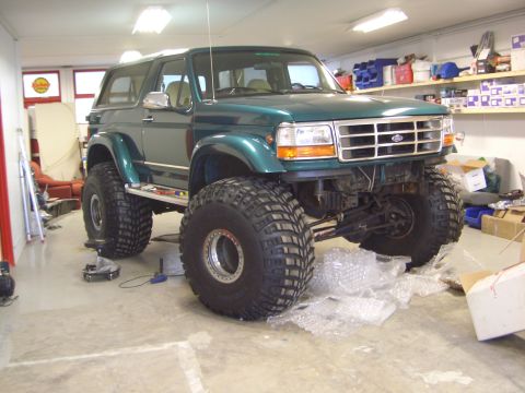 1996 Ford Bronco - Modified green Ford Bronco with large off-road tires sits in a workshop.