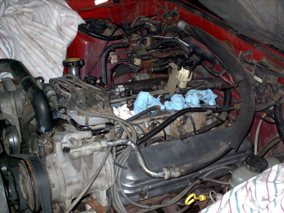 Engine bay mid-repair with cylinder head exposed and rags stuffed in spark plug holes