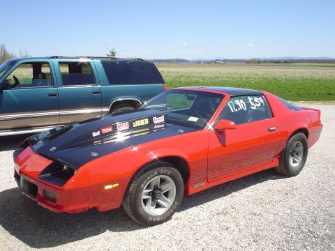 1985 Chevrolet Camaro - 1985 Chevrolet Camaro drag car with aftermarket hood and racing numbers on window.