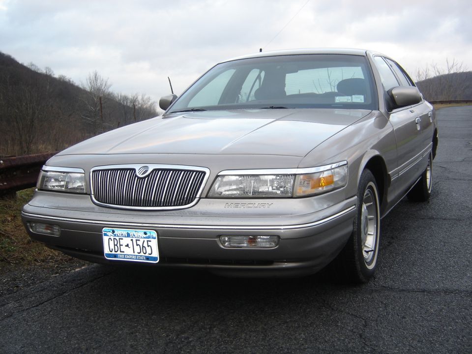 Tan Mercury Grand Marquis sedan, front three-quarter view, New York plate CBE-1565, parked by guardrail