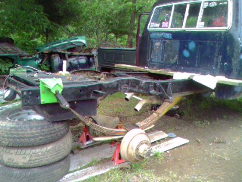 1977 Ford F-250 - The rear chassis of a truck is elevated on jack stands, with a disassembled green truck body in the background.
