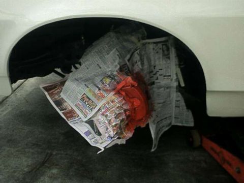 1976 Ford Ranchero - A red brake caliper is covered with newspaper inside the wheel well of a white vehicle.