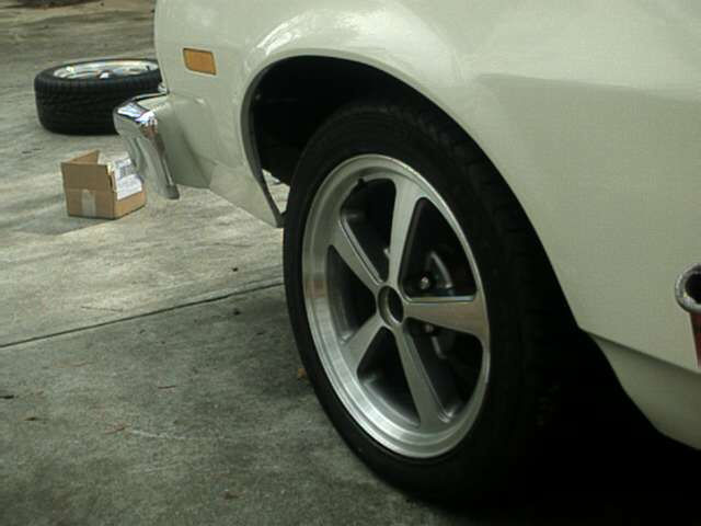 White car front wheel with five-spoke mag wheel and red caliper, stock wheel on ground
