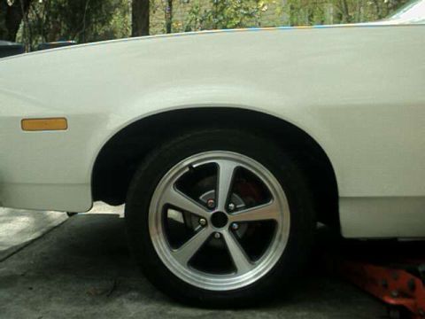 1976 Ford Ranchero - A close-up view of a white car's front fender and wheel, showing custom alloy rims and a hint of the brake system.