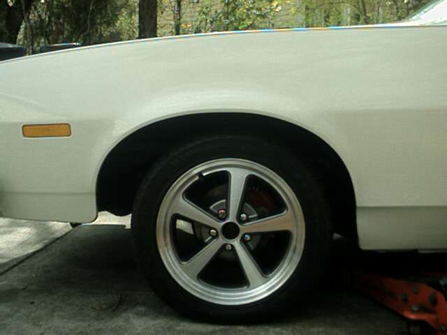 White car fender and wheel with five-spoke alloy rim, amber turn signal, and red brake caliper