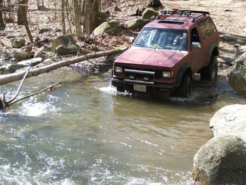 1996 Ford Bronco - This vehicle is navigating a rocky stream bed, with a fallen tree partially obstructing the path.
