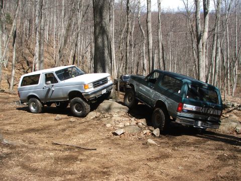 1996 Ford Bronco - Two Ford Broncos navigate a challenging off-road course through a forest.