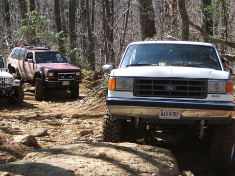 1996 Ford Bronco - A white 1996 Ford Bronco navigates a rocky trail, with another off-road vehicle visible behind it.