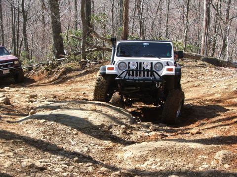 1996 Ford Bronco - Two off-road vehicles navigate a challenging rocky path through a wooded area.