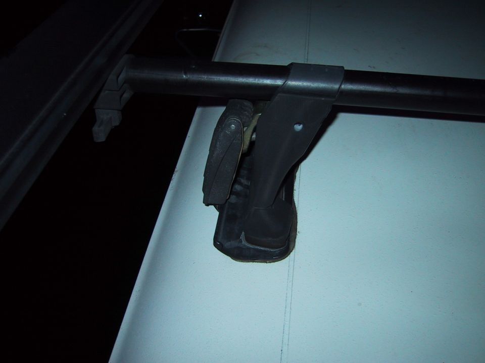 Close-up of a roof rack crossbar tower clamped over a roof rail with a glove resting on it